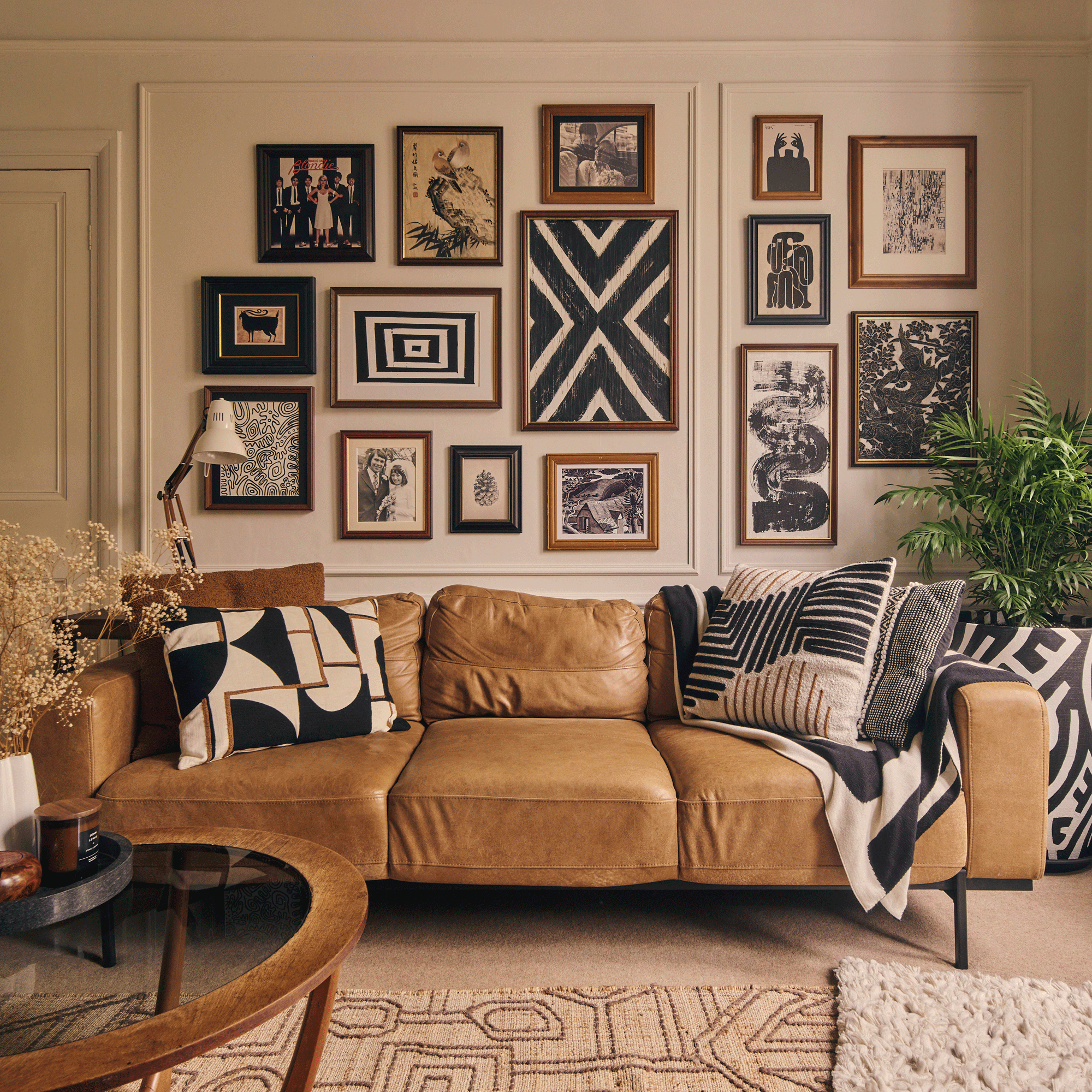 a living room with a brown leather sofa with a bold gallery wall behind it and lots of cushions and throws to match