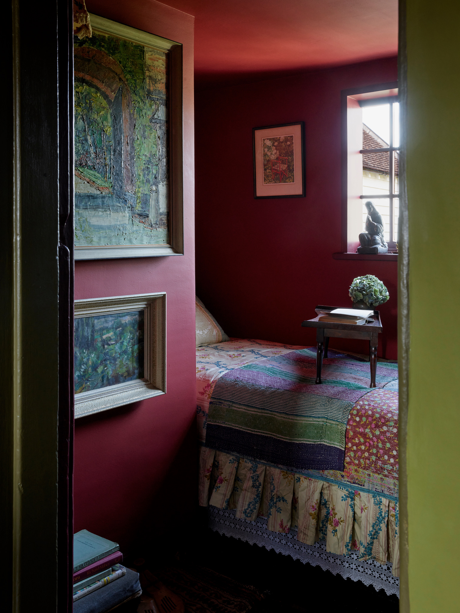 colorful small bedroom with bed nook, small window, art on walls, patchwork quilt, and a table on the bed with a book