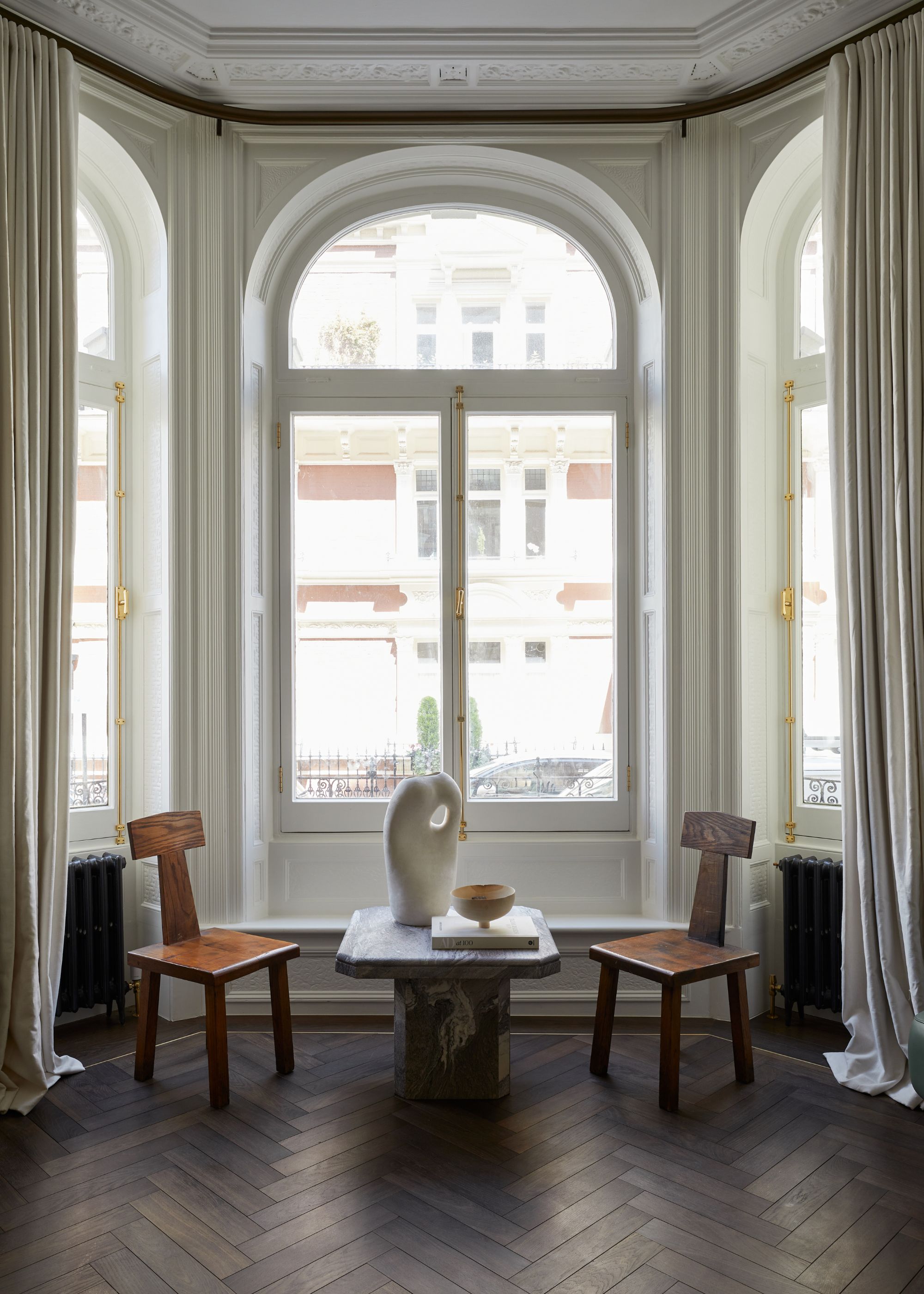 living room with dark parquet flooring, large bay window with arched glass, white walls and cream curtains