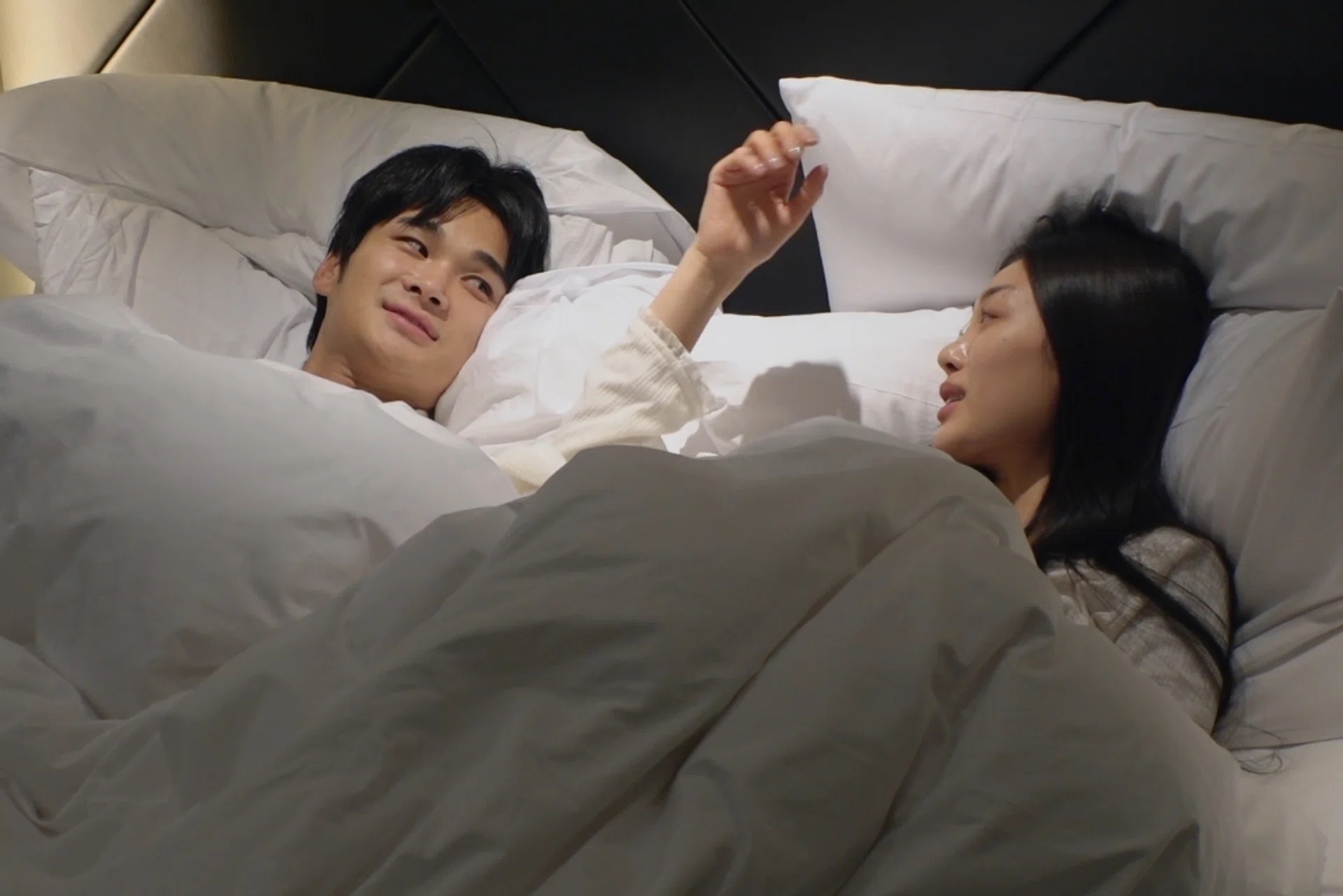 A Korean man and woman talk while lying in a fluffy white bed, in the Netflix dating show 'The Love Lab'.