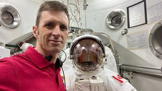 an astronaut standing in front of a spacesuit. a canadian flag is on the shoulder of the spacesuit