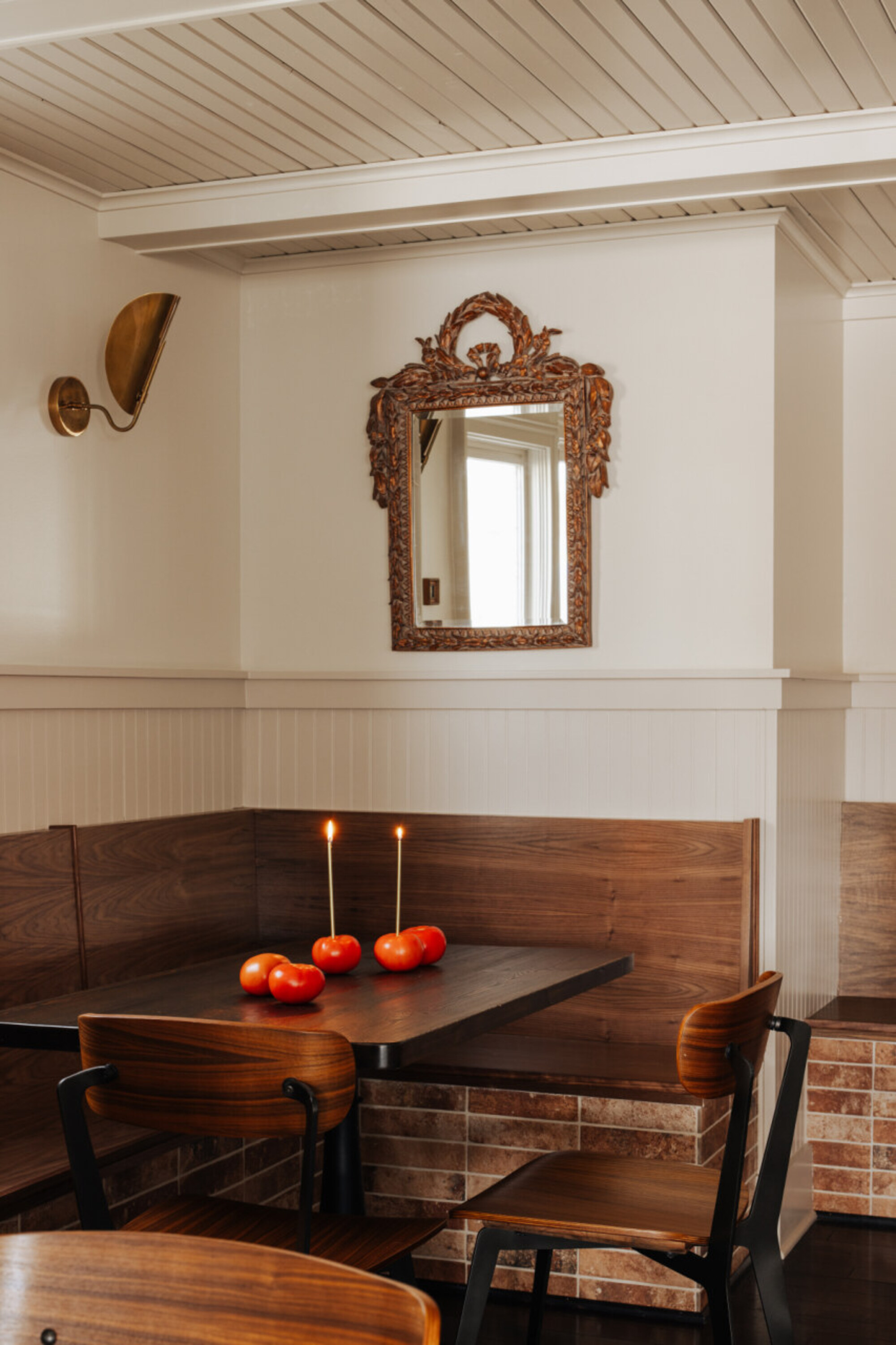 a timber and brick dining nook with tomato centrepieces and thin pillar candles