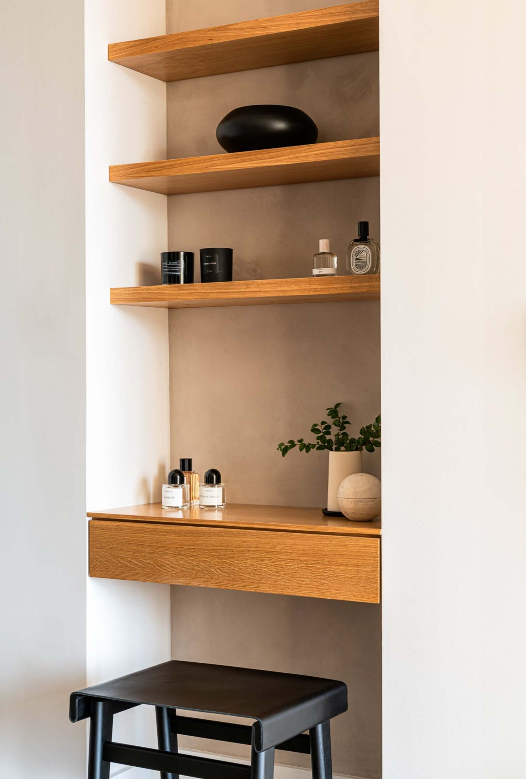 built-in vanity with floating timber shelves and a desk that has a drawer and stool, and pot plant and perfumes