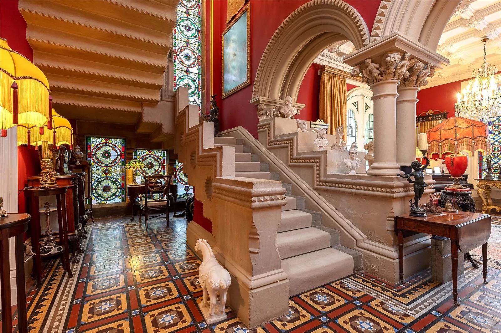 View of the staircase hall at Northorpe Hall, showing a stone staircase, arches, columns and stained glass