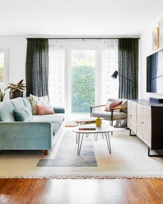 living room with tv, turquoise blue sofa, coffee table nest, sideboard, black drapes, armchair, rug