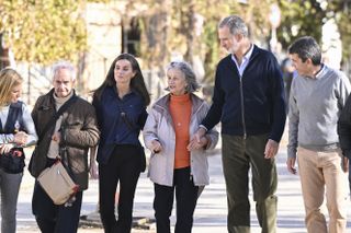 Queen Letizia and King Felipe linking arms with flood victims walking down a sunny street