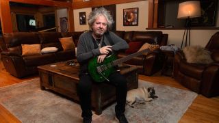 Steve Lukather at home cradling a guitar with a pug at his feet 