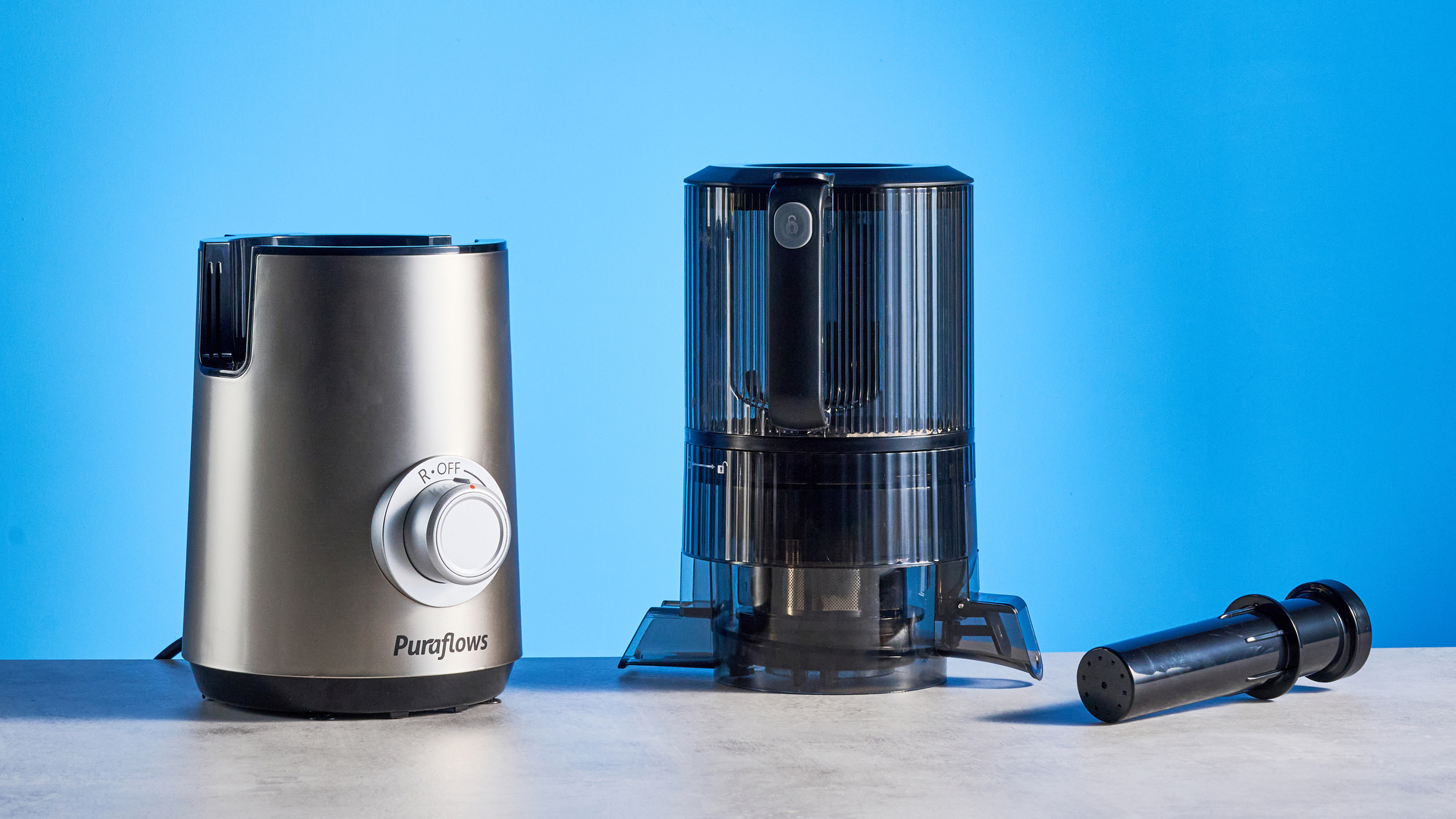 Puraflows Auramist Cold Press Juicer and accessories photographed in front of a blue background