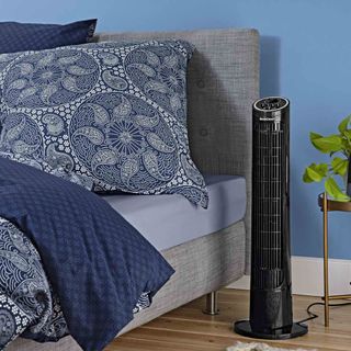 grey bed with blue designed cushion and black tower fan