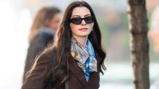 A photo of Anne Hathaway in a brown jacket, scarf and sunglasses