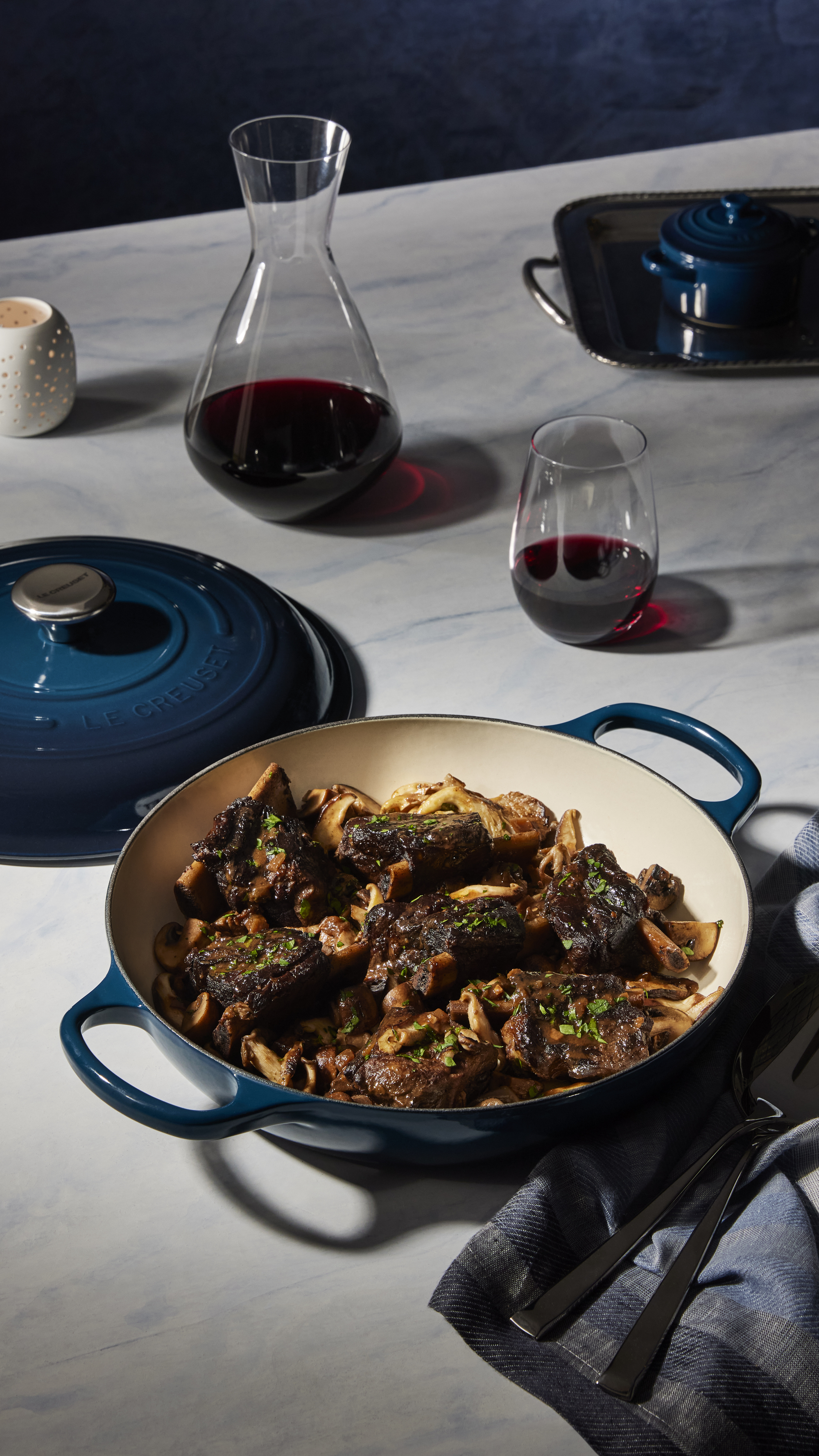 table set with le creuset noir collection, decanter or red wine with glass of wine, silver tray, blue napkin and meal in the casserole