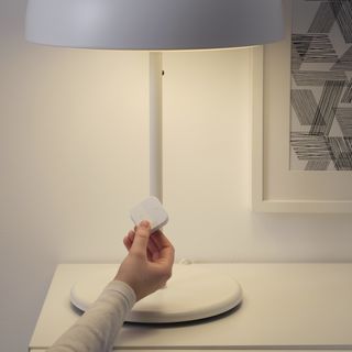 A white lamp with a hand controlling it via a wireless dimmer switch