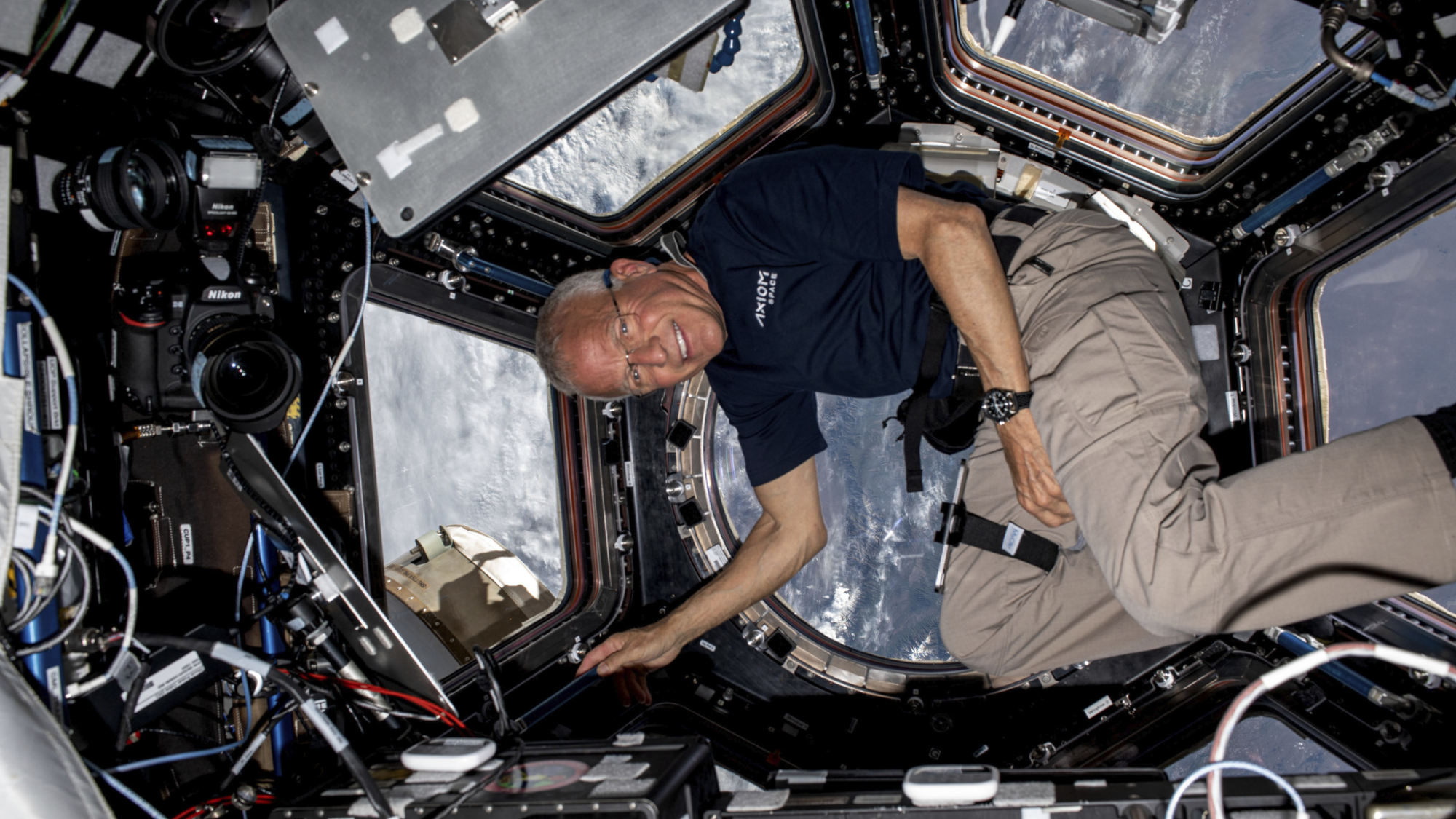 Ax-2 pilot John Shoffner floating in weightlessness with Earth behind in the window.