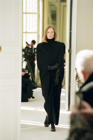 Woman on The Row runway wearing black dress and black leather gloves