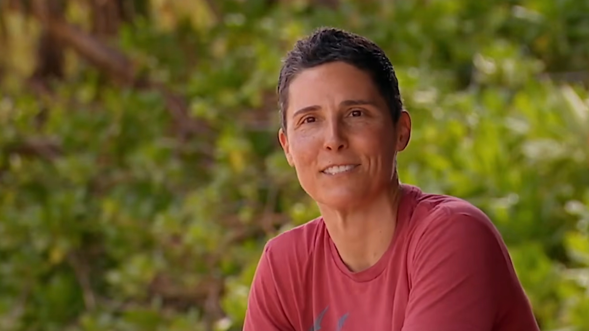 Kristin wears a red shirt and talks during a confessional in the woods on Survivor.
