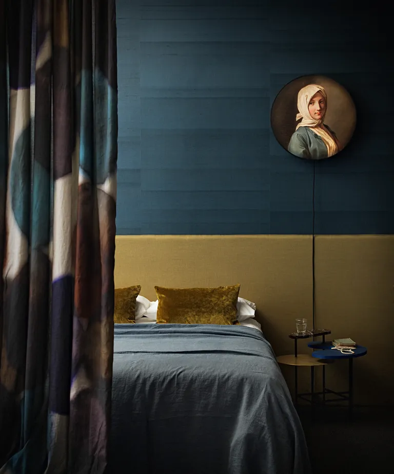 A bedroom with dark teal walls and a yellow ochre bedhead