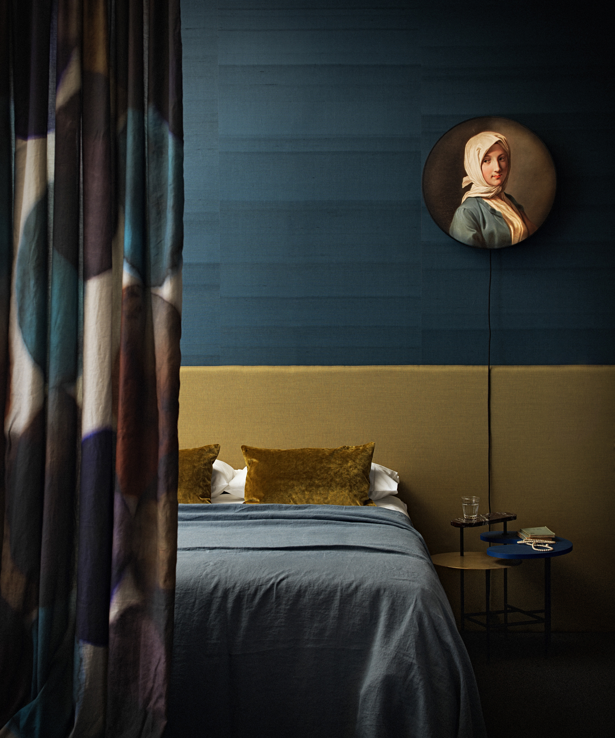 An example of dark bedrooms showing a bedroom with dark teal walls and a yellow ochre bedhead