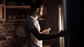 Man looks in fridge, it is dark around him