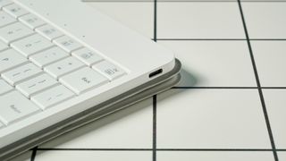 the usb charging port of a white, lightweight tablet keyboard made by mokibo rests upon a white tiled table with a blue background