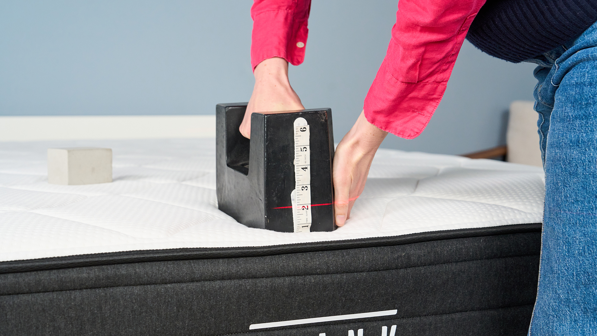 Mattress tester Nicola Appleton places a 25kg weight on the edge of the Plank Firm Luxe mattress in our Sleep Lab