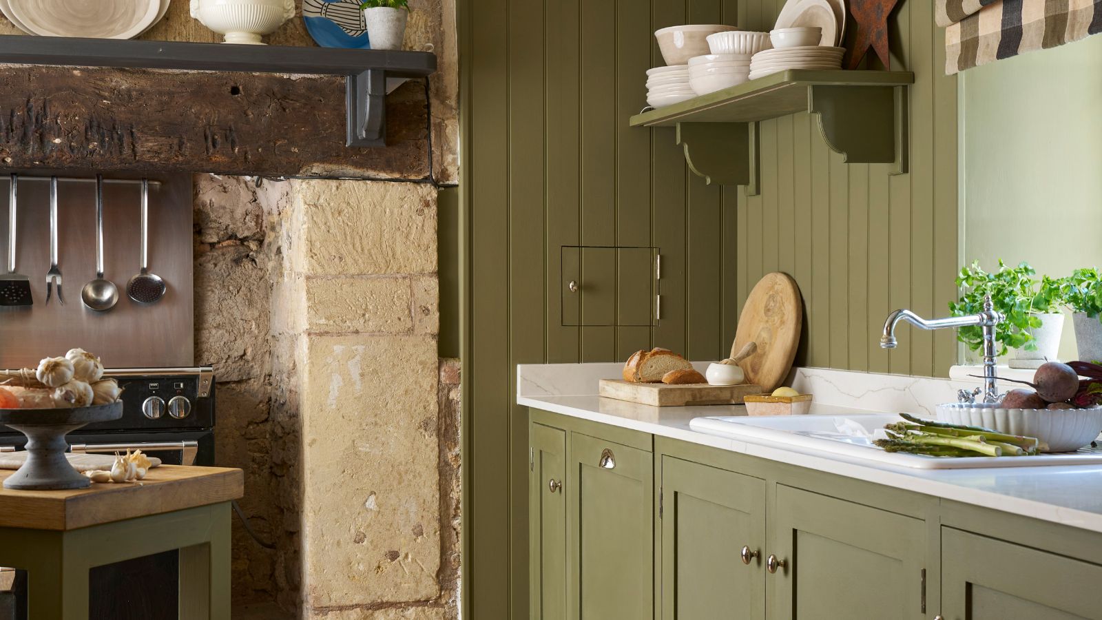 A green painted kitchen, with a traditional brick fireplace surrounding a stove. White worktops. 