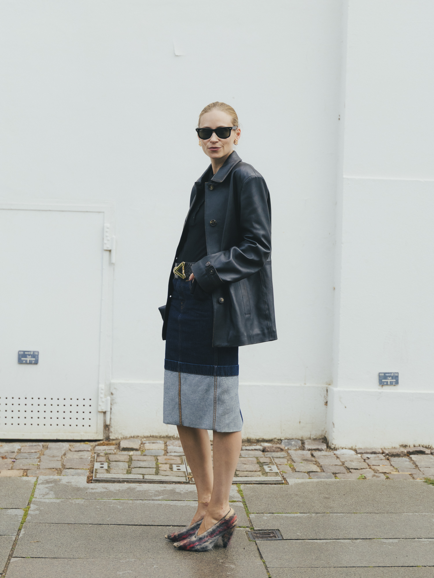 a woman wears a black leather jacket, denim pencil skirt, and plaid heels.