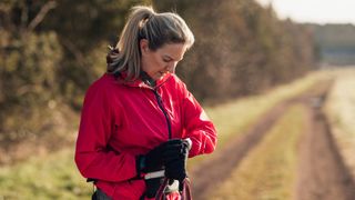 Woman looking down at wrist with fitness tracker alongside countryside road on a walk