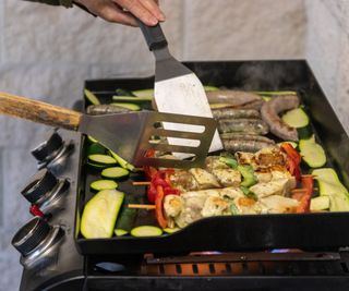 Cooking sausages, skewers and zucchini in a pan