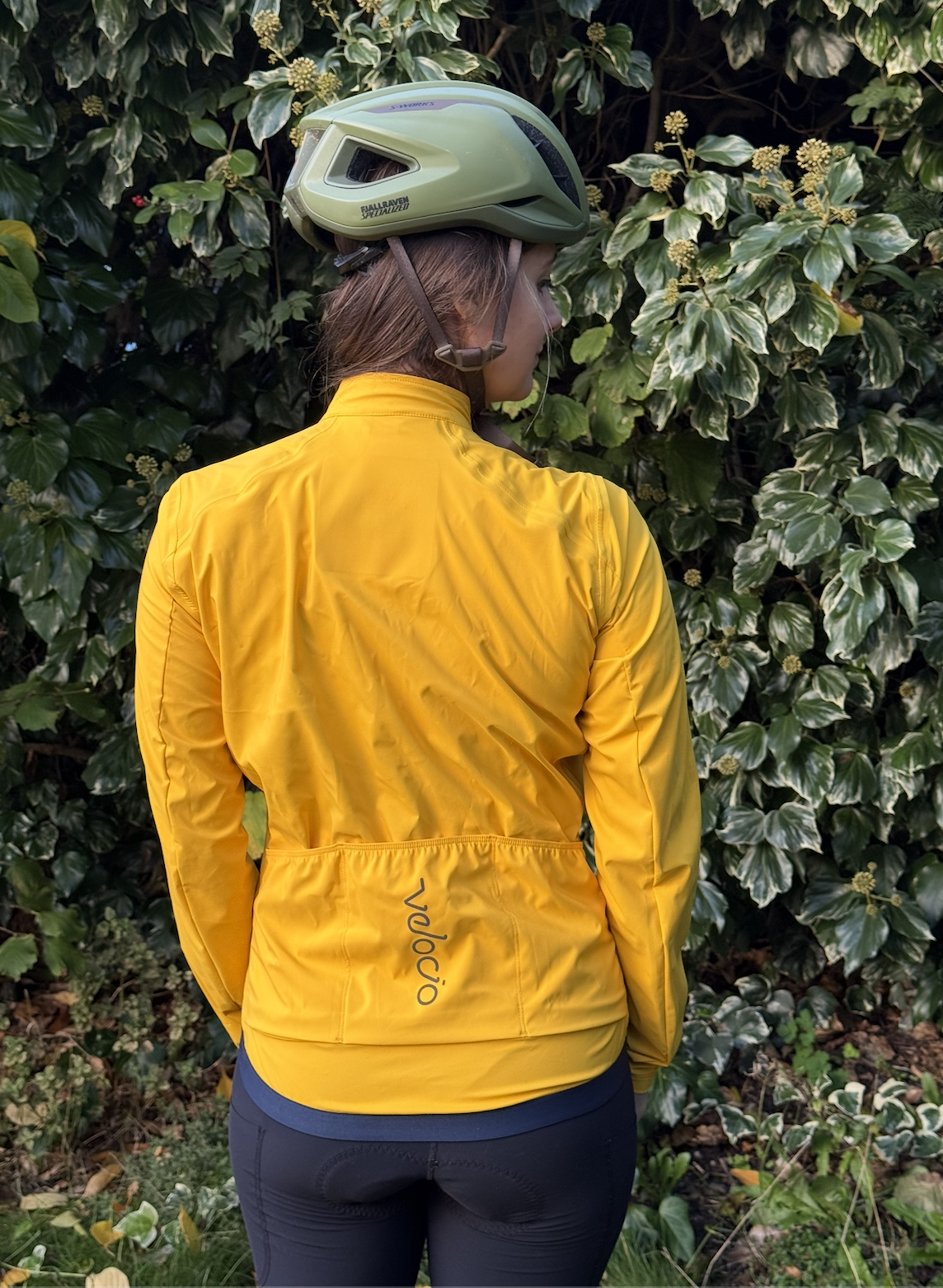 Immy stands with her back to the camera, showing the bright yellow jacket with small navy detail and pocket.