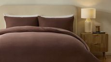 brown muslin bedding set in neutral bedroom with fluted timber side table with lamp, candle, and book