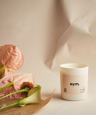 A cream jar with a candle inside, on a crumbled paper background. Lily flowers laying beside it.