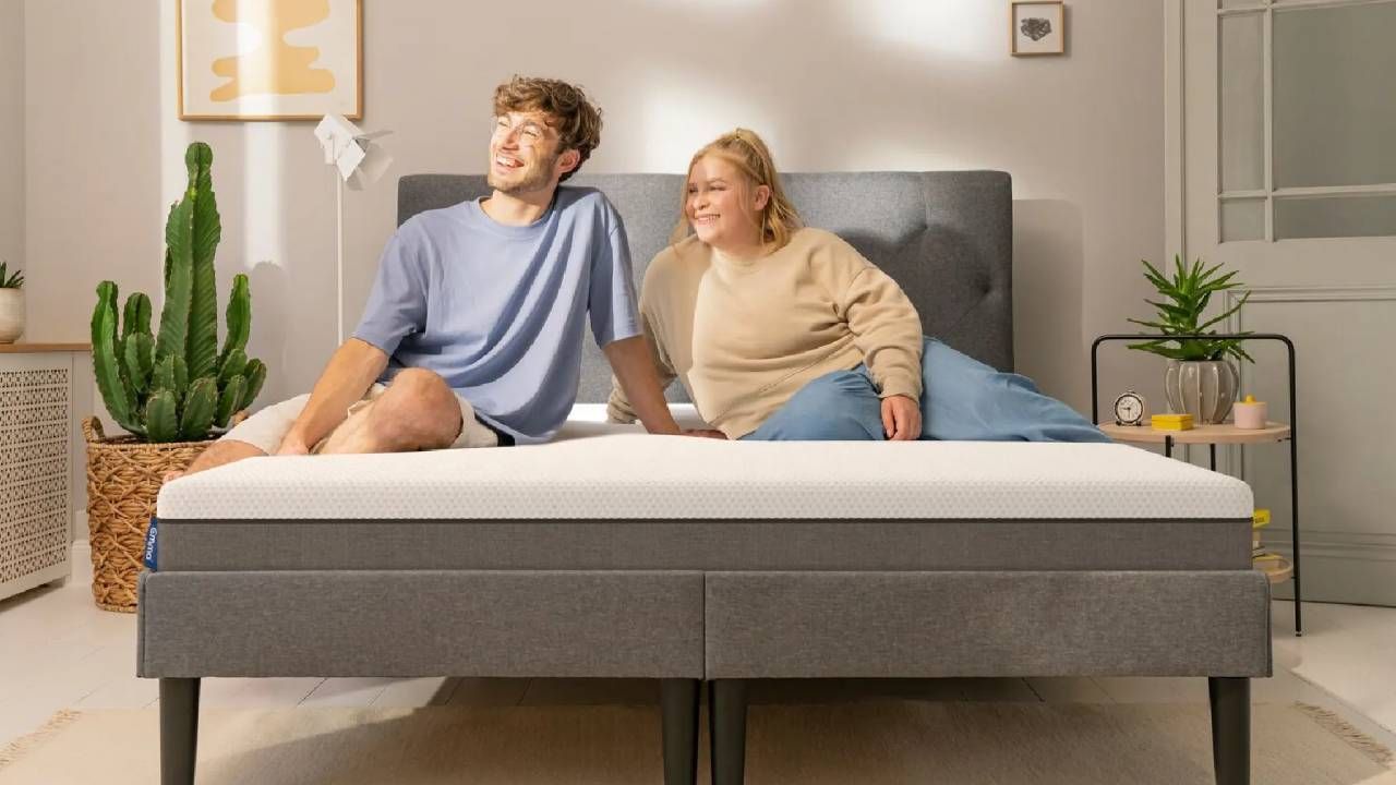 A couple smiling while sitting on an Emma mattress