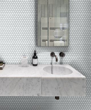 Small white bathrom tiles above a marble sink boost space in a tiny bathroom.