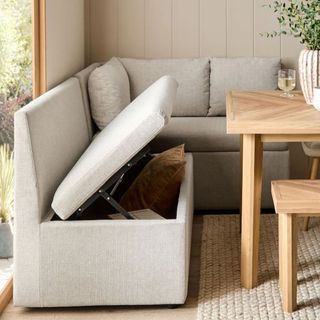 Corner banquette seating, upholstered in light linen fabric, lifted up to reveal hidden storage 