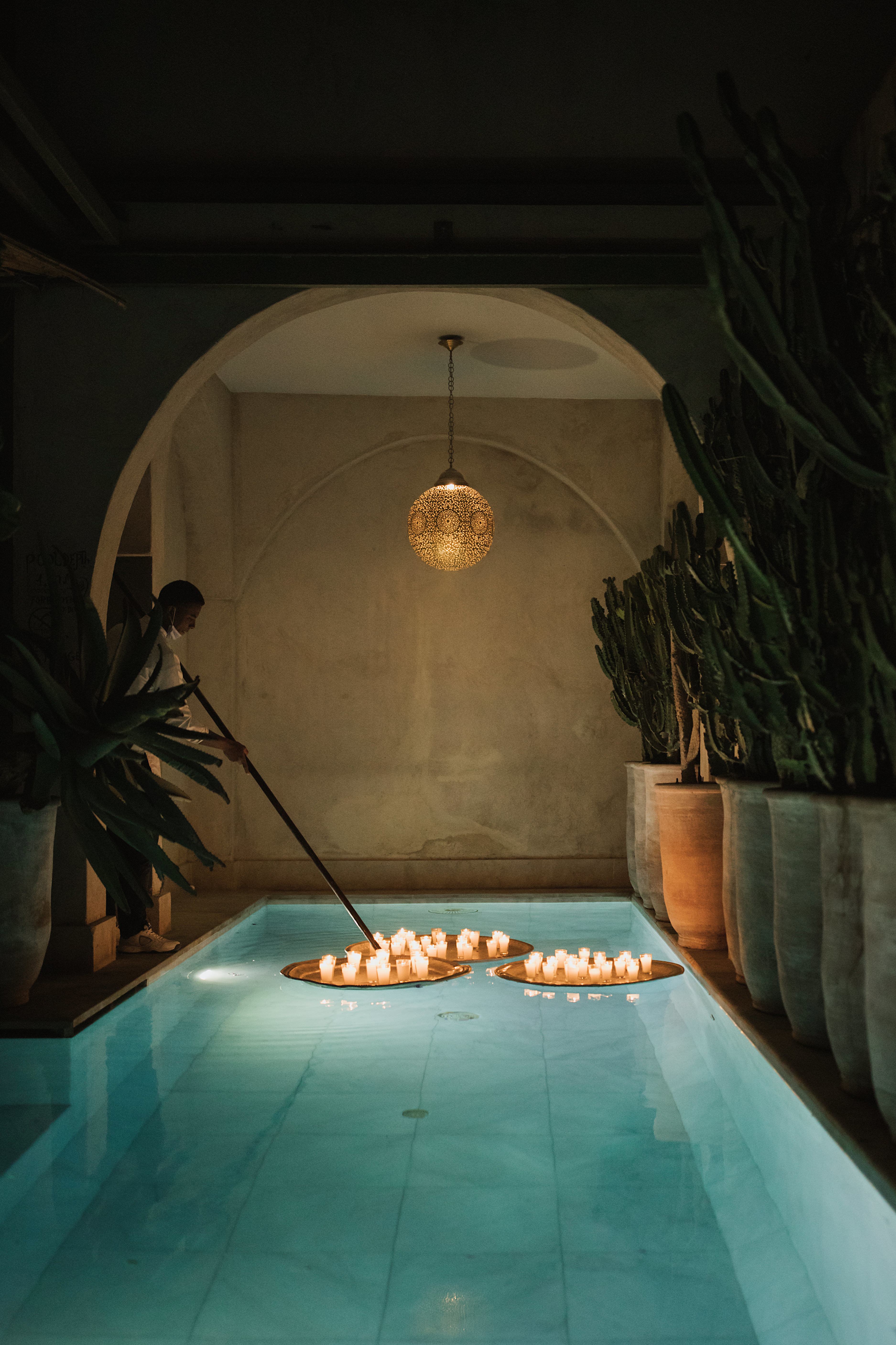 A candle-lit spa pool is being decorated by a member of the hotel staff as golden light spreads through this arched room.