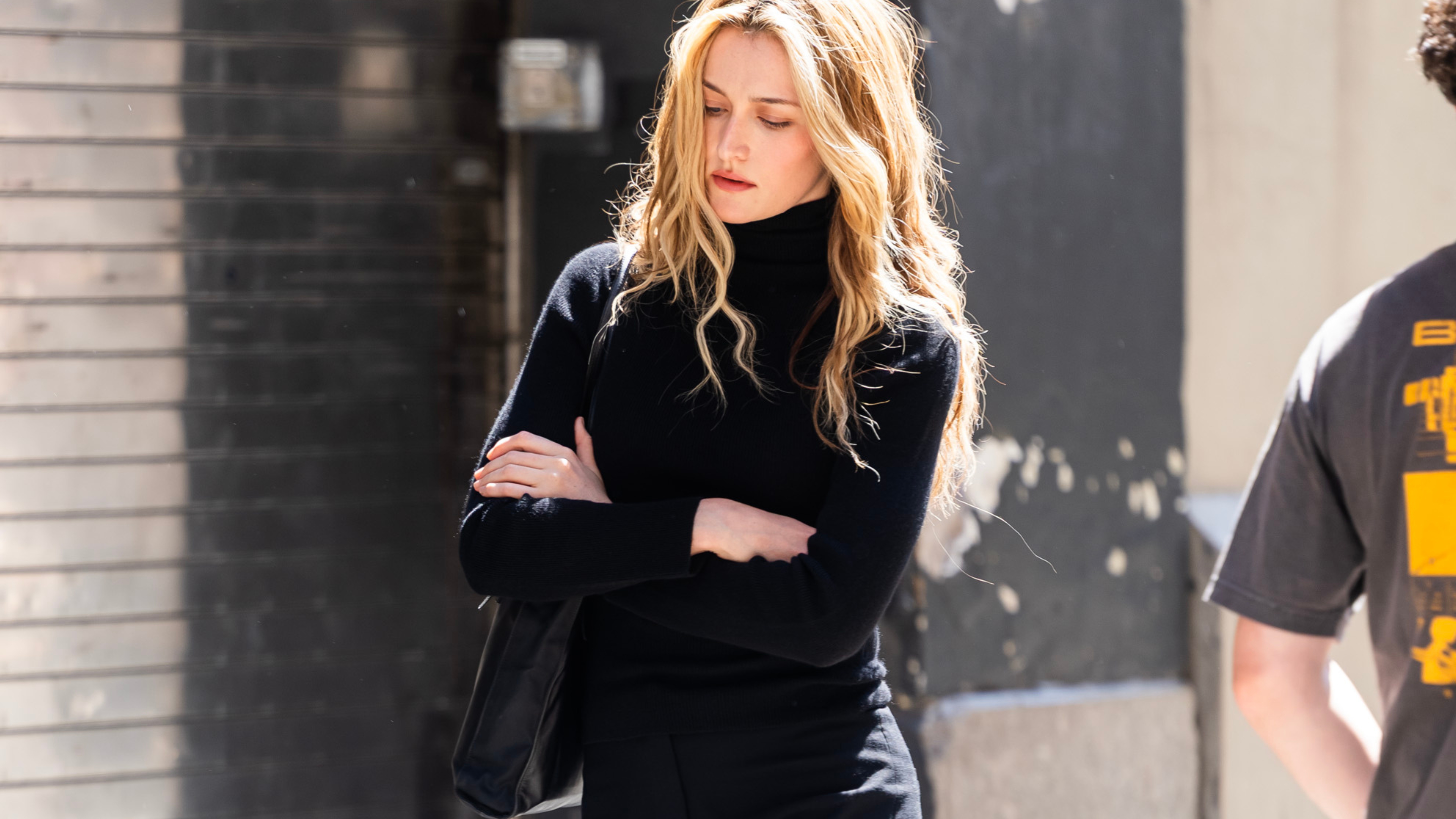 Sarah Pidgeon in character as she portrays Carolyn Bessette-Kennedy in the upcoming series American Love Story, wearing black cropped trousers, black loafers and a black roll neck knit