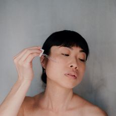 Woman with dark hair and short fringe applying the best serum for oily skin to her face