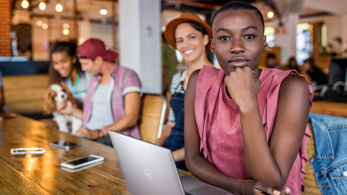 Lady looks into camera with her laptop in front of her and a group of collaborators in the background