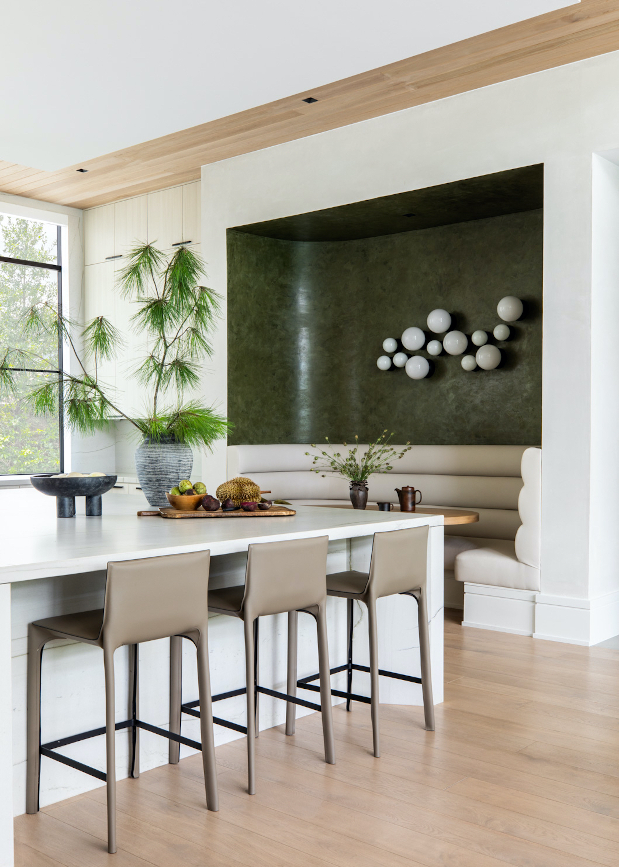 A modern kitchen with an island in the middle as well as bar stools beside it. In one corner of the kitchen there is also a built in seating area with a table