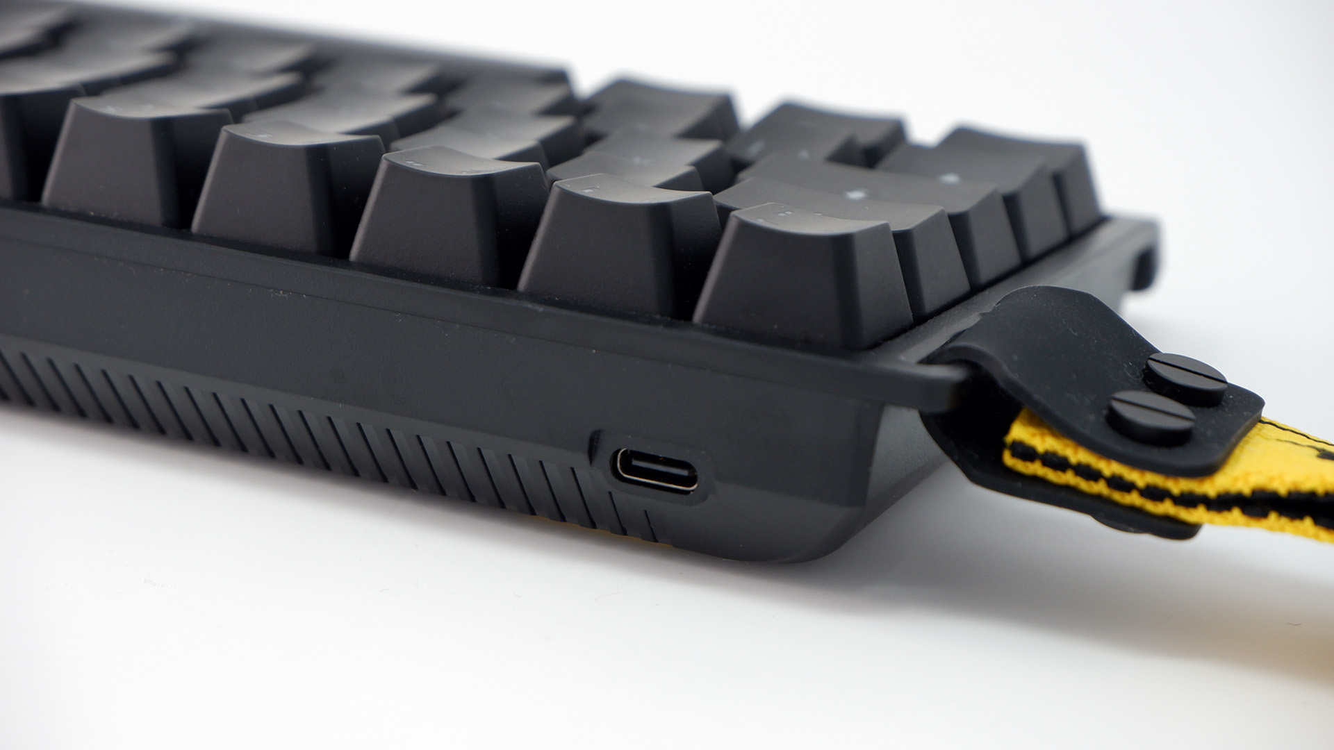Wooting 60HE gaming keyboard pictured with yellow wrist strap attached.