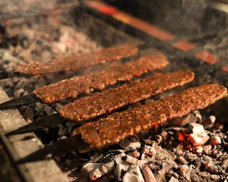 A row of Turkish adana kebabs on manga barbeque made from minced lamb and assortment of spices cooked over charcoals