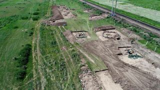 A bird's-eye view of a grassy field that has exposed brown dirt with graves where the archaeologists excavated.