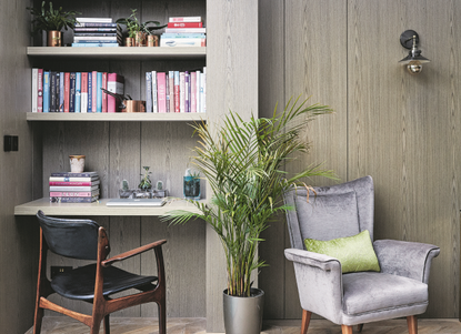 A home office with book shelves, an arm chair, and a fern