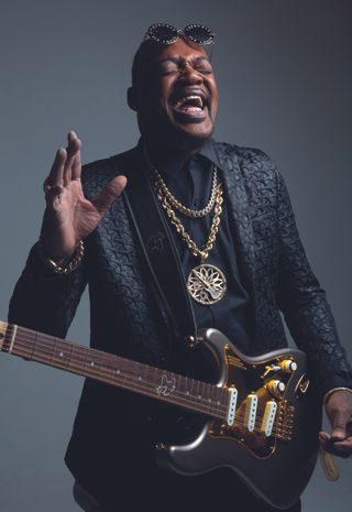 Eric Gales stands in a photo studio holding his signature Eric Gales Magneto RawDawg electric guitar