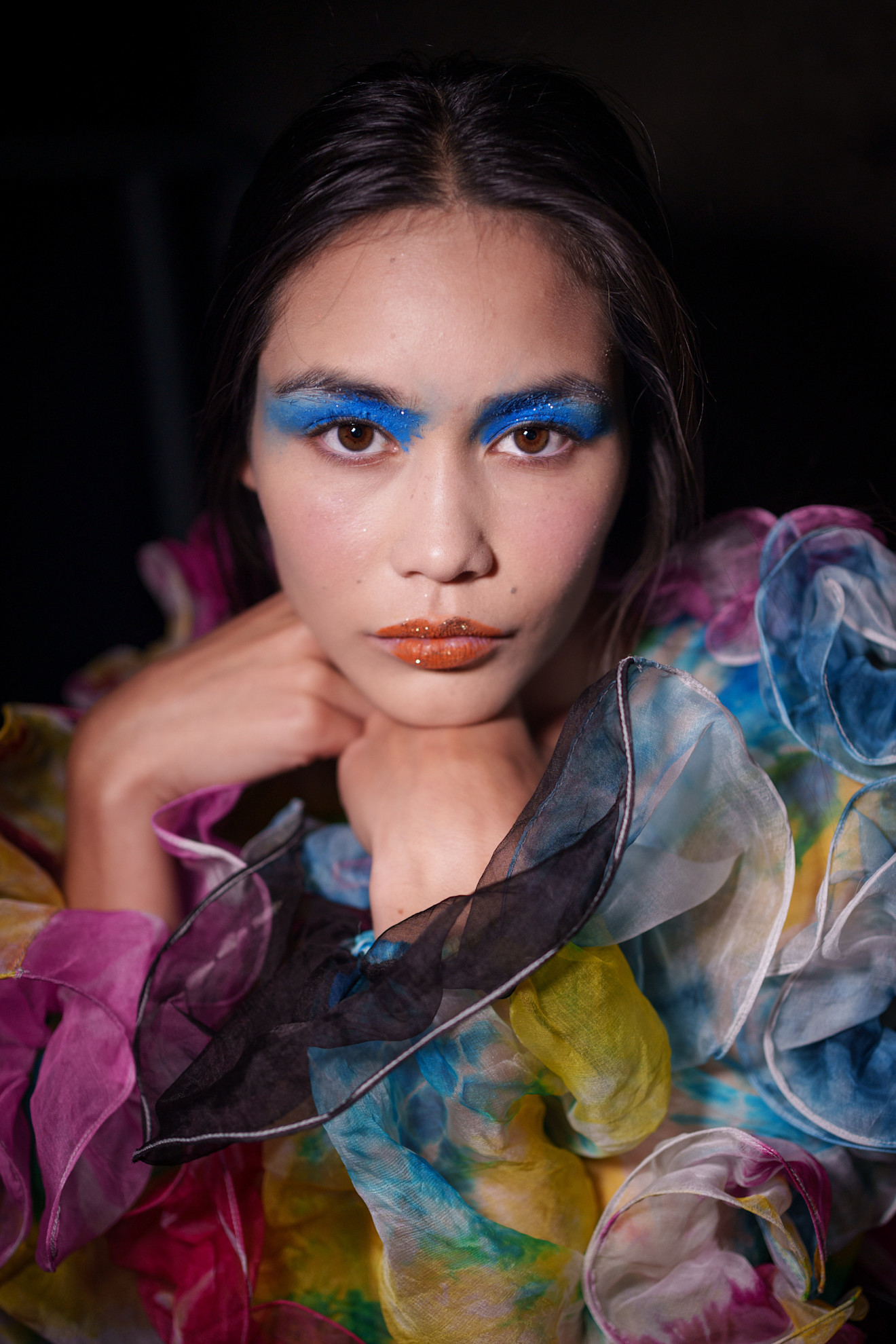 A model at Ashish SS26 with bright blue glittery eyeshadow and glittery orange lips