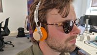 A man wearing orange headphones, plays a brown guitar, in an office. 
