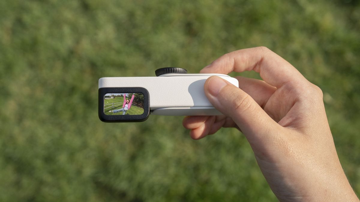 Insta360 Go 3S Retro edition, with the thumb-szied action camera slotted into the Retro Bundle's viewfinder case, held by a user, looking down into the finder