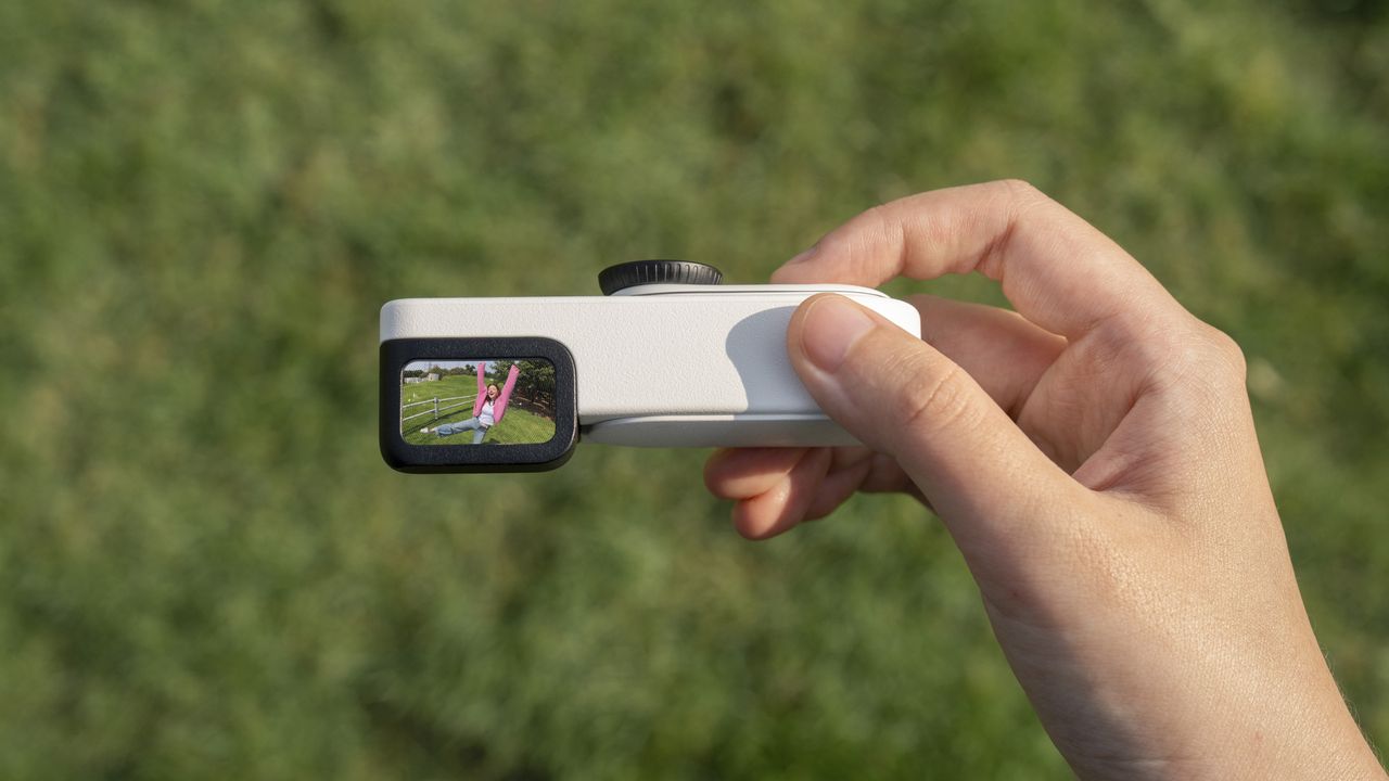Insta360 Go 3S Retro edition, with the thumb-szied action camera slotted into the Retro Bundle's viewfinder case, held by a user, looking down into the finder