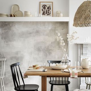 A dining room with a single wall shelf, a grey wall and a wooden table with black chairs