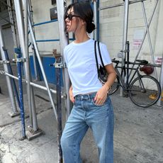 style influencer Mimi Nguyen poses on a NYC sidewalk wearing a cool denim outfit with black sunglasses a white T-shirt, black shoulder bag, and baggy Madewell jeans